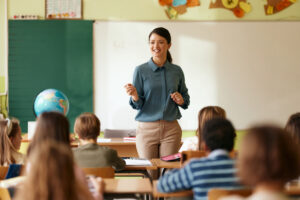 Happy female teacher talking to group of her students during a class at elementary school. Copy space.